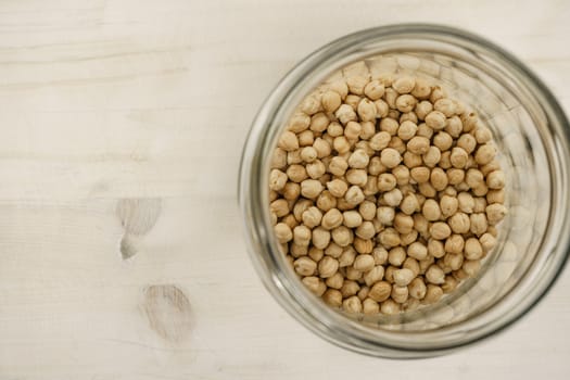 Back to the natural vegan food theme copy space: top down flat lay view of a big glass jar filled of dried chickpeas on light wooden table background