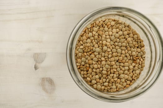 Back to the natural vegan food theme copy space: top down flat lay view of a big glass jar filled of dried lentils on light wooden table background