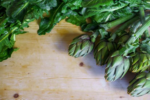 Close up of a bunch of fresh artichokes freshly picked by the farmer laid on a wooden table and illuminated by sunlight, vegan and mediterranean cuisine ingredients