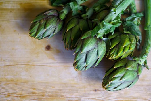 Close up of a bunch of fresh artichokes freshly picked by the farmer laid on a wooden table and illuminated by sunlight, vegan and mediterranean cuisine ingredients