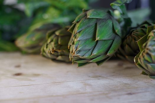 Close up of thorns leaves of the artichokes freshly picked by the farmer laid on a wooden table and illuminated by sunlight, vegan and mediterranean cuisine ingredients