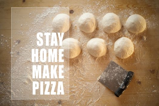 Stay at home for coronavirus covid-19 lockdown concept: white text stay home make pizza in frame on top view of leavened dough portions ready to bake on a light wooden table dusted with flour