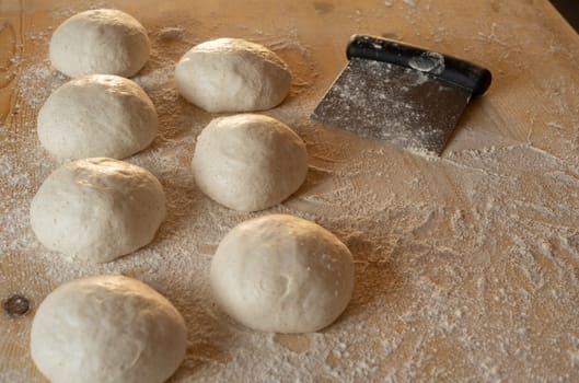 Stay at home for coronavirus covid-19 lockdown concept: make pizza at home. Low angle view of leavened dough portions ready to bake on a light wooden work table dusted with flour