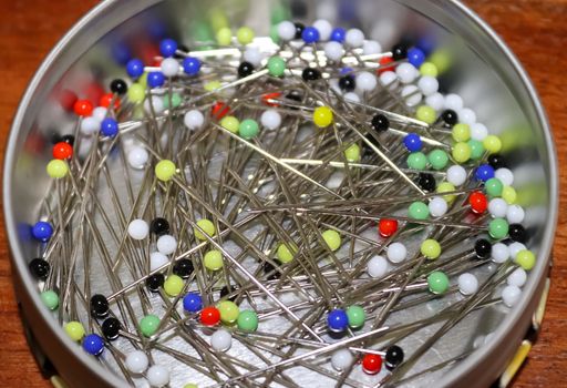 Close up view on lots of sewing pins with colored heads in a metal box