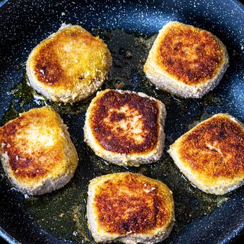 Breaded chicken cutlets, heated in a ceramic black skillet with vegetable oil. The process of frying steaks. Traditional cuisine.