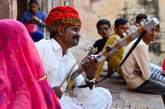 Jodhpur, Rajasthan, India, circa 2020. Sarangi player performing in his traditional dress and head gear pagdi in Rajasthan as tourists enjoys his performance in Mehrangarh Fort.