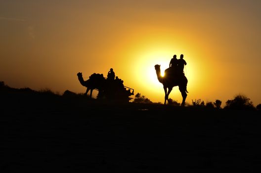 Silhouette of a camel cart and camel carrying tourists in Sam sand dunes, Jaisalmer. Located in the midst of the Thar Desert, these sand dunes are amongst the most famous ones in Rajasthan, India