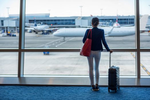 Businesswoman traveling in airport. Woman looking through the window at tarmac and planes waiting for flight. Business travel concept.