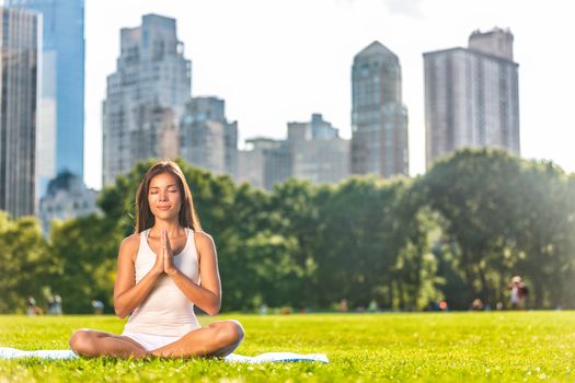 New York City Central Park yoga girl relaxing meditating woman in meditation in outside in summer. Beautiful young mixed race Asian Caucasian model sitting in lotus pose in grass.