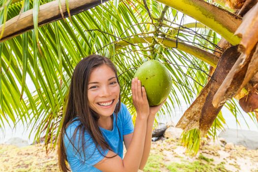 Tahitit tourist woman on coconut farm showing natural fruit hanging on palm tree. Happy Asian girl on tropical vacation holidays.