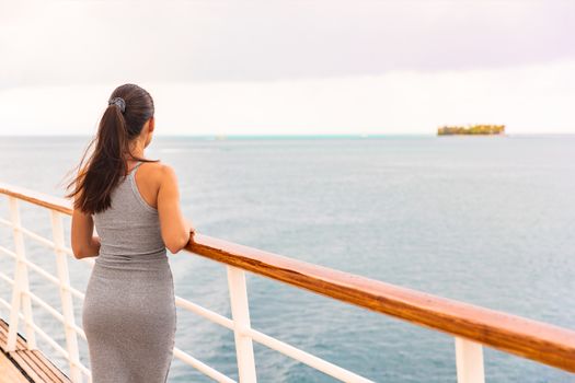 Luxury cruise ship vacation on tropical ocean travel - Young tourist woman watching sunset on deck of cruising boat. Tahiti destination, island in background.