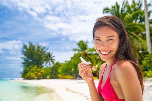 Fresh coconut slice Asian woman eating healthy snack on beach holiday. Summer vacation in Tahiti smiling girl holding fruit cut by local at tropical travel destination. Coco water, popular food trend.