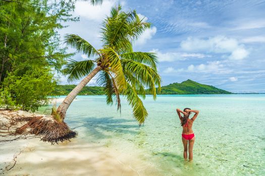 Paradise luxury beach vacation in Tahiti island French Polynesia woman relaxing in red bikini bathing suit swimming in turquoise perfect water. View of slim body from behind.