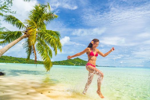 Travel Vacation beach woman laughing having fun splashing in water on Tahiti paradise beach on Bora Bora on holidays. Happy girl wearing Bikini in Tahiti, French Polynesia.