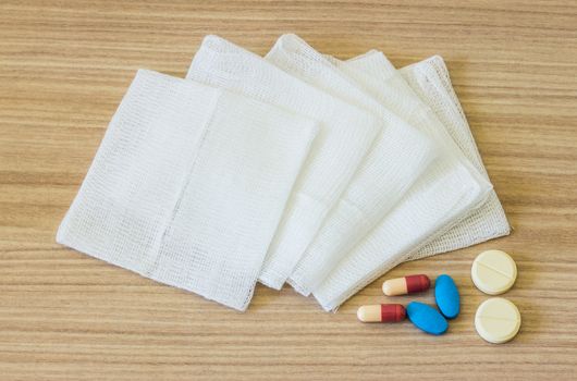 white gauze pads and medicines on wooden background
