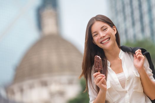 Business woman eating ice cream in Hong Kong. Young businesswoman enjoying ice-cream on at stick walking outside smiling happy in central Hong Kong. Mixed race Chinese Asian / Caucasian model