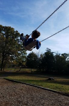 boy child swinging high on swing at playground