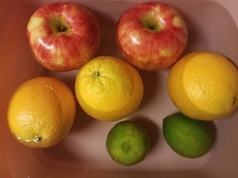 apples and oranges and limes floating in water in pink container