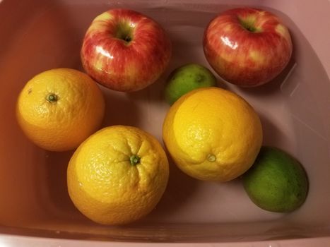 apples and oranges and limes floating in water in pink container