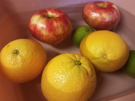 apples and oranges and limes floating in water in pink container