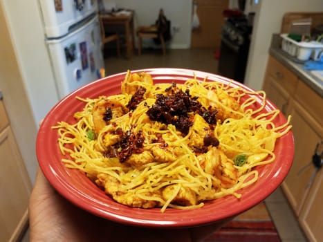 spicy Chinese noodles with chili sauce in red bowl in kitchen