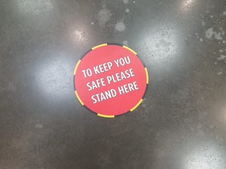 red to keep you safe please stand here social distancing sign on floor