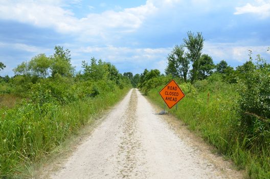 orange road closed ahead sign with path or trail