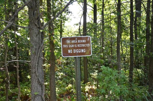 the area behind this sign is restricted no digging sign with trees in forest or woods