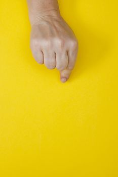 Hand with clenched fingers in a pinch on a yellow background