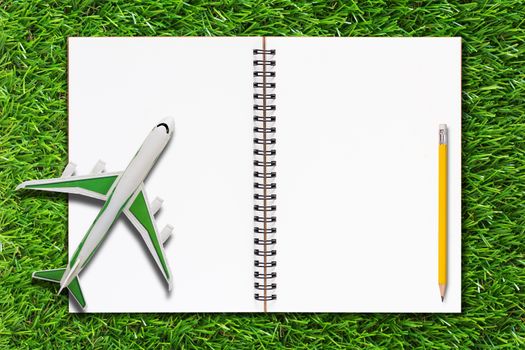 Travel concept, open notebook and yellow pencil on green grass background