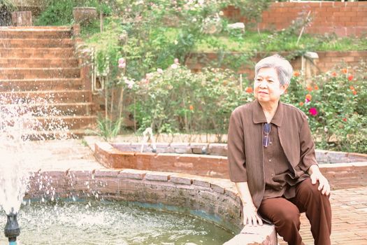 elder woman resting in rose flower garden. asian elderly female relaxing outdoors. senior leisure lifestyle