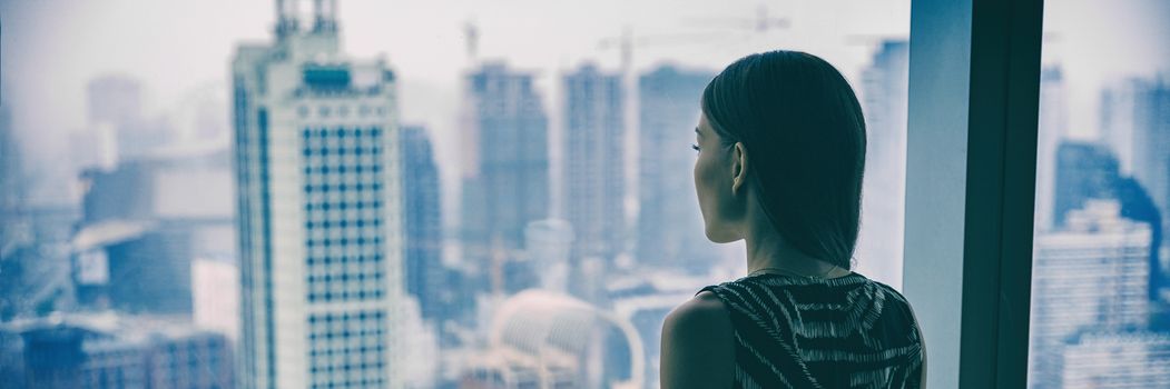 COVID-19 Quarantine mental health. Woman self isolated at home pensive looking out of high rise building window at city skyline thinking of relationship, employment, coronavirus. Panoramic banner.