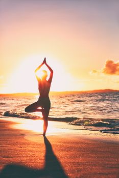 Yoga wellness retreat class on morning sunrise beach landscape. Silhouette of girl standing in tree pose meditation vertical background.