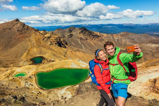 New Zealand Tongariro Alpine Crossing Hiking tourists couple selfie at Emerald Lakes. Happy backpackers tramping taking phone photo of themselves at volcanic mountains. Tramping track of New Zealand.