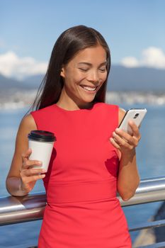 Happy Asian business woman on coffee break smiling texting sms message mobile data phone or reading online. City urban businesspeople lifestyle.