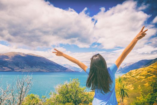 New Zealand travel wanderlust happy tourist woman with v sign hand up at Wanaka lake landscape summer destination. Adventure young girl excited traveling the world alone.