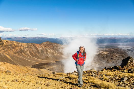 New Zealand Tongariro Alpine Crossing Hiking trek hiker woman with bag and outdoor jacket tramping in volcanic steam vents fumaroles background. Summer travel vacation adventure trekking girl hike.