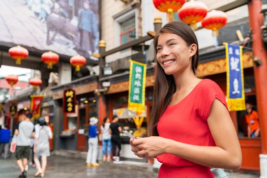 China food market tourist woman walking using phone Beijing hutong street travel vacation adventure. City lifestyle young Asian girl. Asia summer travel destination. Girl traveling in Asia chinatown.