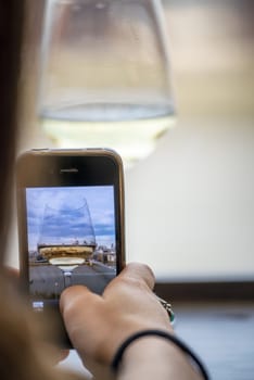 Taking a drink with wine glass and smartphone in front of city skyline.