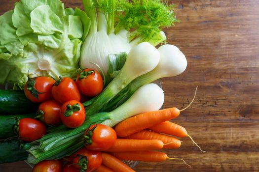 Healthy nutrition with fresh raw vegetables: flat lay top view of a group of salad ingredients, lettuce, tomatoes, cucumbers, fennel, spring onions, and carrots on a wooden table copy space