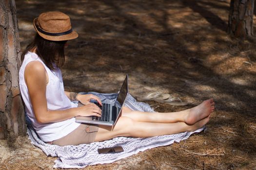 Freelance woman working in vacation on the laptop sitting in a pine forest on the sea, smart working lifestyle concept theme and life choice