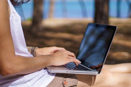 Close up of freelance woman working in vacation on the laptop sitting in a pine forest on the sea, smart working lifestyle concept theme and life choice