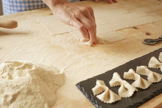 Close up process of homemade vegan farfalle pasta with durum wheat flour. The cook shapes the dough on the wooden cutting board, traditional Italian pasta, the woman cooks the food in the kitchen