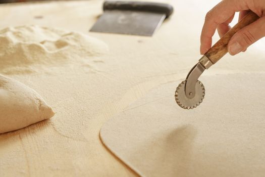 Close up process of homemade vegan farfalle pasta with durum wheat flour. The cook uses the rolling cutter to cut the dough, traditional Italian pasta, the woman cooks the food in the kitchen