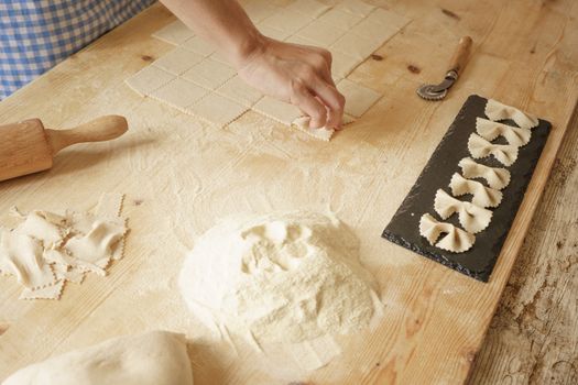 Close up process of homemade vegan farfalle pasta with durum wheat flour. The cook shapes the dough on the wooden cutting board, traditional Italian pasta, the woman cooks the food in the kitchen
