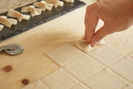 Close up detail of process of homemade vegan farfalle pasta with durum wheat flour. The cook kneads the dough on the wooden cutting board, traditional Italian pasta, the woman cooks the food