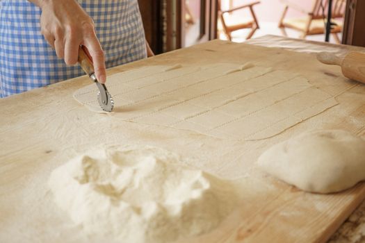 Close up process of homemade vegan farfalle pasta with durum wheat flour. The cook uses the rolling cutter to cut the dough, traditional Italian pasta, the woman cooks the food in the kitchen