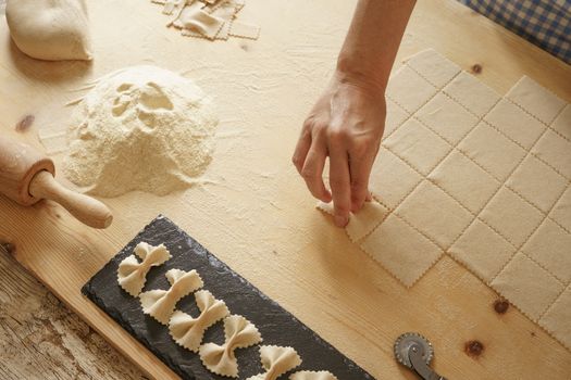 Close up process of homemade vegan farfalle pasta with durum wheat flour. The cook shapes the dough on the wooden cutting board, traditional Italian pasta, the woman cooks the food in the kitchen