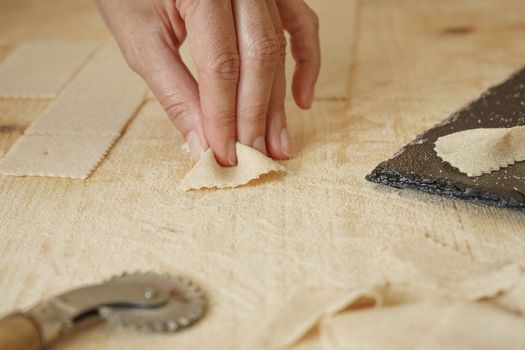 Close up macro detail of process of homemade vegan farfalle pasta with durum wheat flour. The cook kneads the dough on the wooden cutting board, traditional Italian pasta, the woman cooks the food