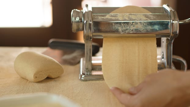 Making fresh homemade pasta: woman's hand pulling out the rolled dough from the manual pasta making machine backlit